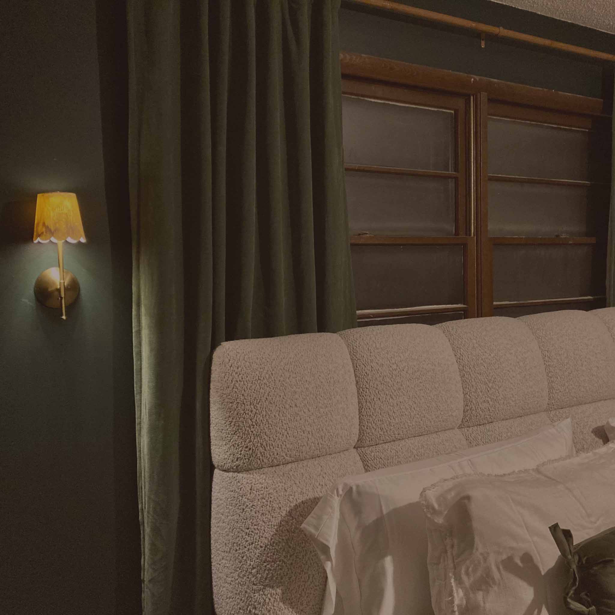 Moody bedroom with green curtains and warm sconce lighting